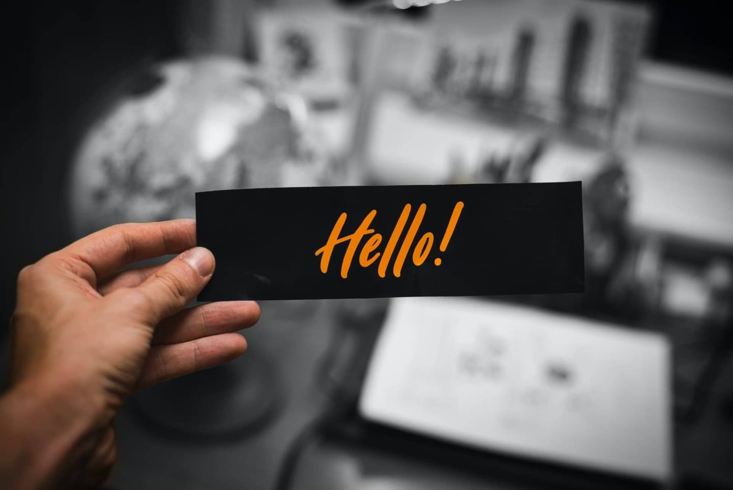 A man holding a small piece of paper with the word hello written on it in orange text